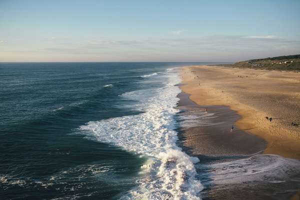 Praia de AndTales com ondas e pessoas em dia de sol.