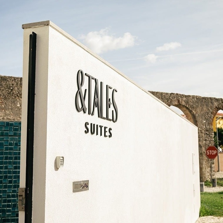 Fachada do AndTales Suites com letreiro e piscina turquesa.