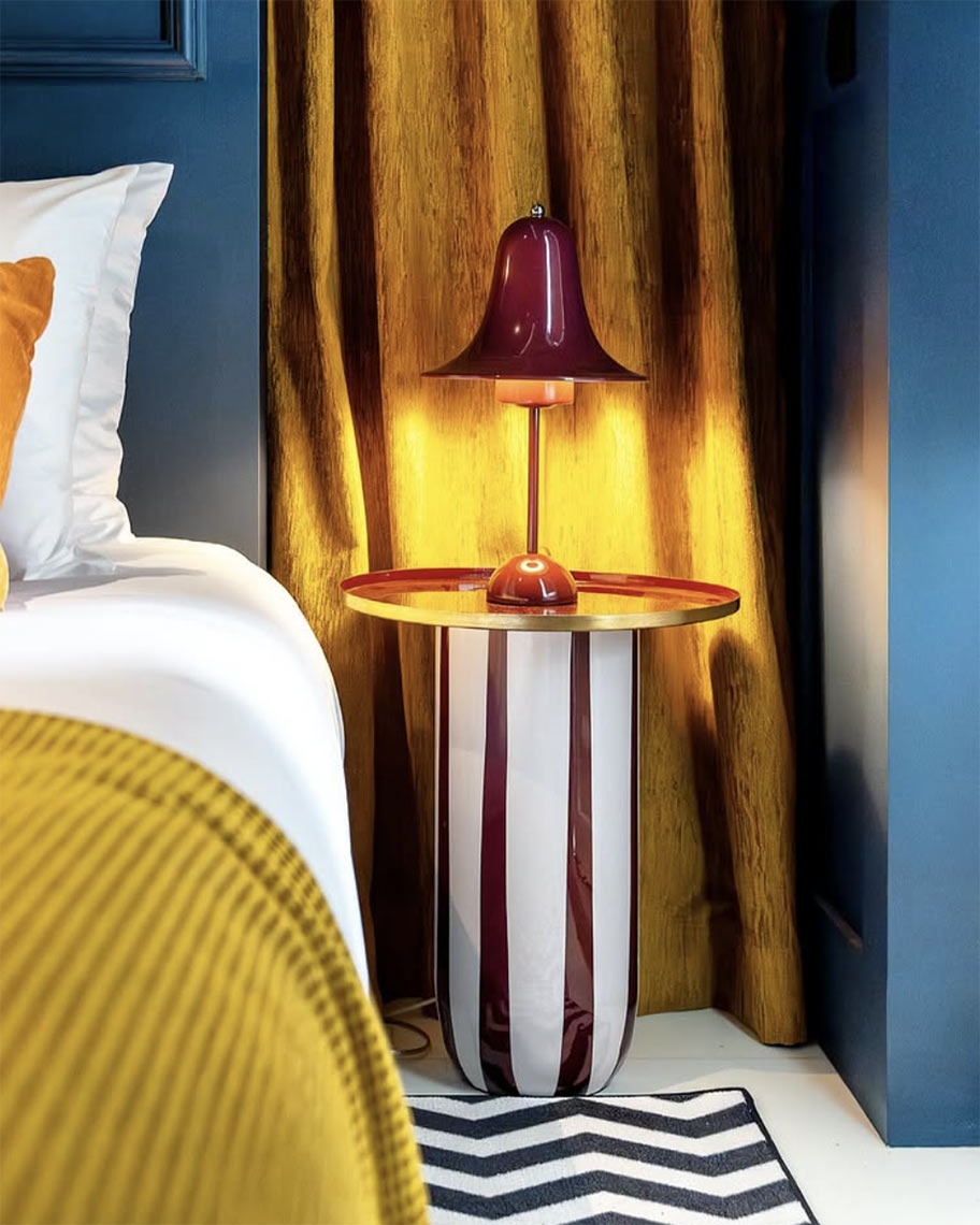 Abajur AndTales e mesa listrada em quarto elegante com cortinas douradas.