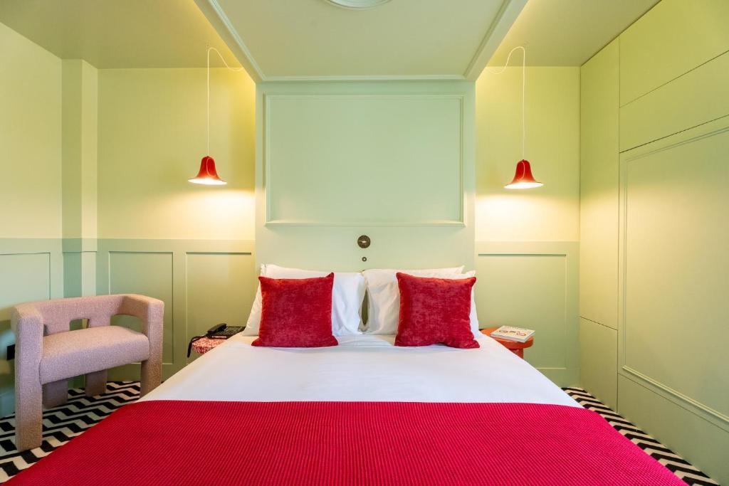 Quarto de hotel AndTales, cama com lençóis brancos, almofadas vermelhas e cobertor, com cadeira e candeeiros de teto vermelhos.
