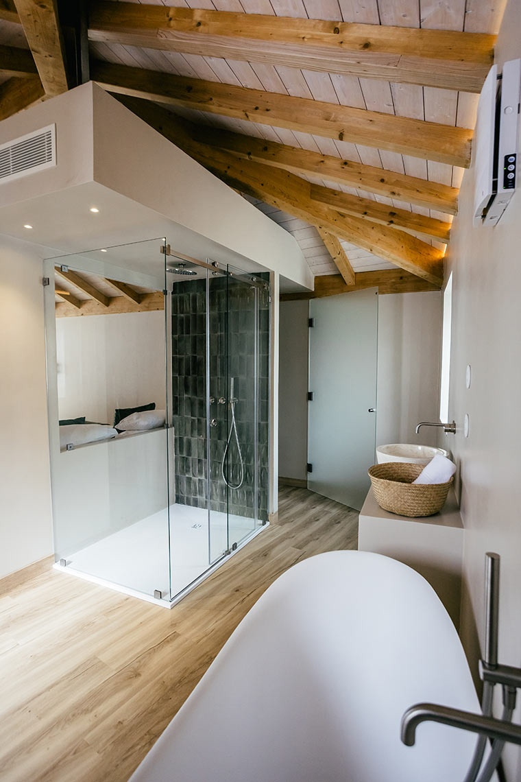 Modern bathroom at AndTales hotel with freestanding tub, glass shower, and exposed wooden beams.