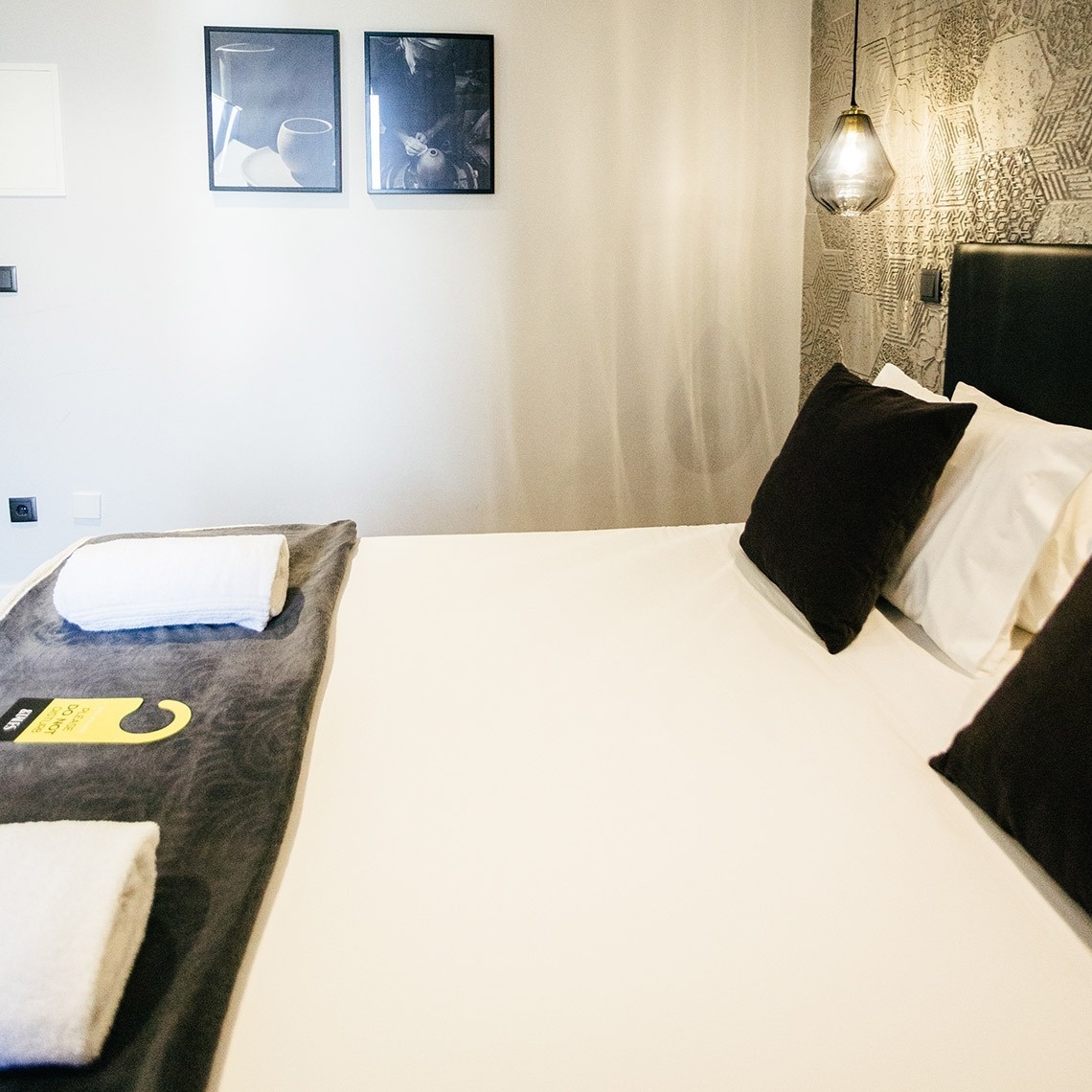 Cama confortável e moderna na AndTales, com toalhas, travesseiros e arte.