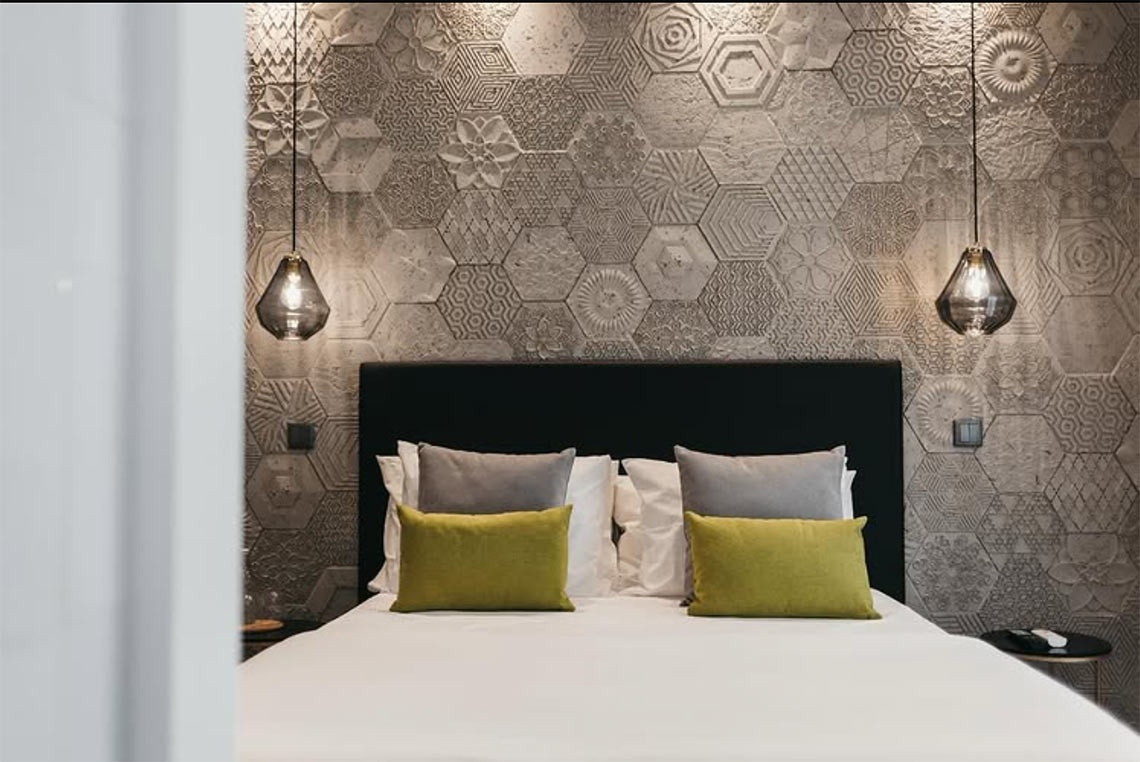 Modern bedroom with textured hexagon tiles, plush pillows, and AndTales pendant lights.