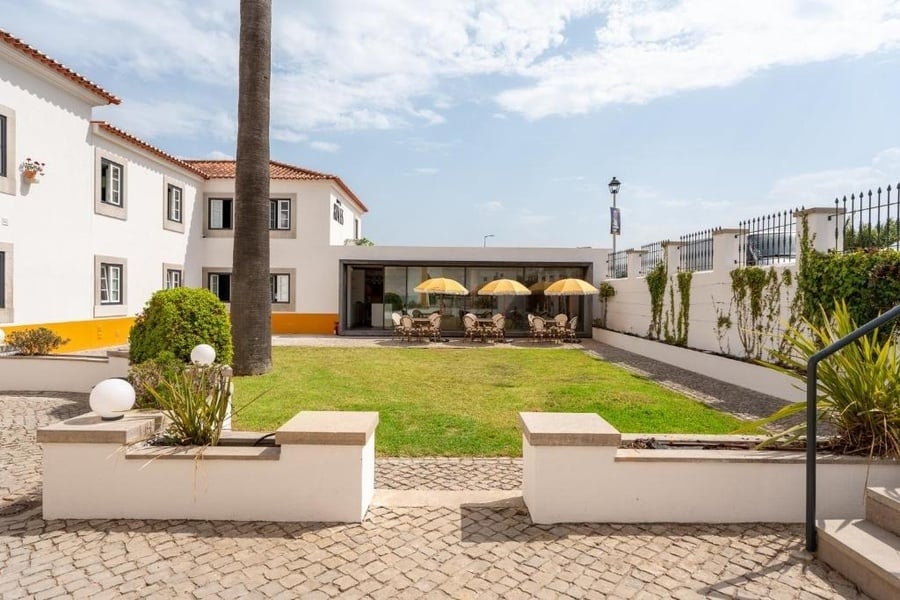 Terraço AndTales: Mesas e guarda-sóis num dia soalheiro, adjacente ao edifício branco.