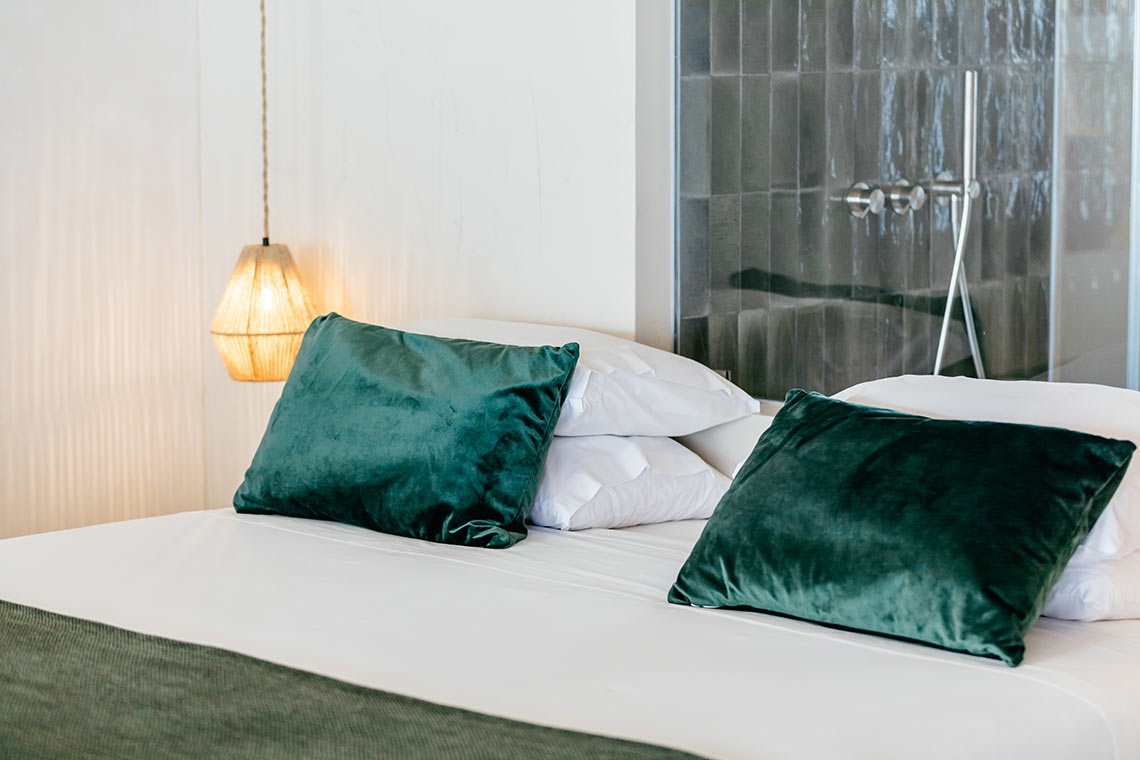 Plush green pillows on a bed with AndTales decor in a modern hotel room.