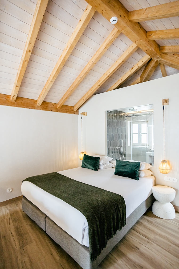 Modern hotel room at AndTales with exposed beams, plush bedding, and glass-enclosed shower.