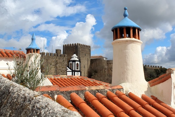 Rua pitoresca com casas brancas floridas em Óbidos, Portugal, inspirada em AndTales.