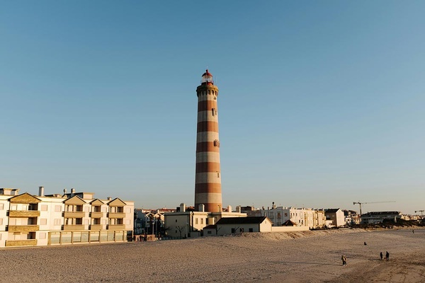 Farol icónico de Aveiro com AndTales. Prédios na praia sob céu azul.
