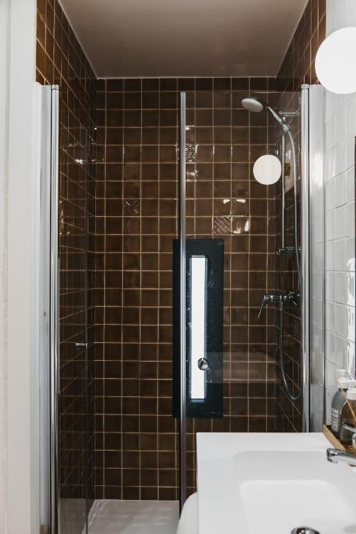 Modern shower at AndTales hotel with sleek glass enclosure and brown tile.