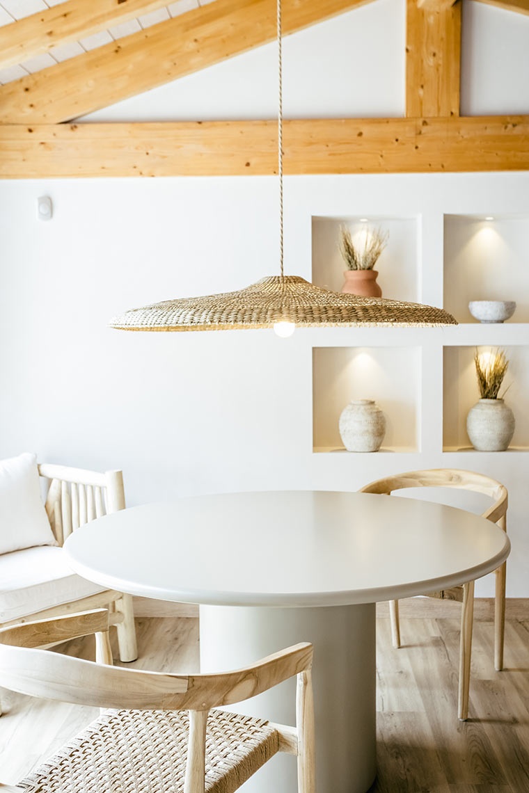 Minimalist dining area at AndTales hotel with round table, wicker pendant light, and natural wood accents.