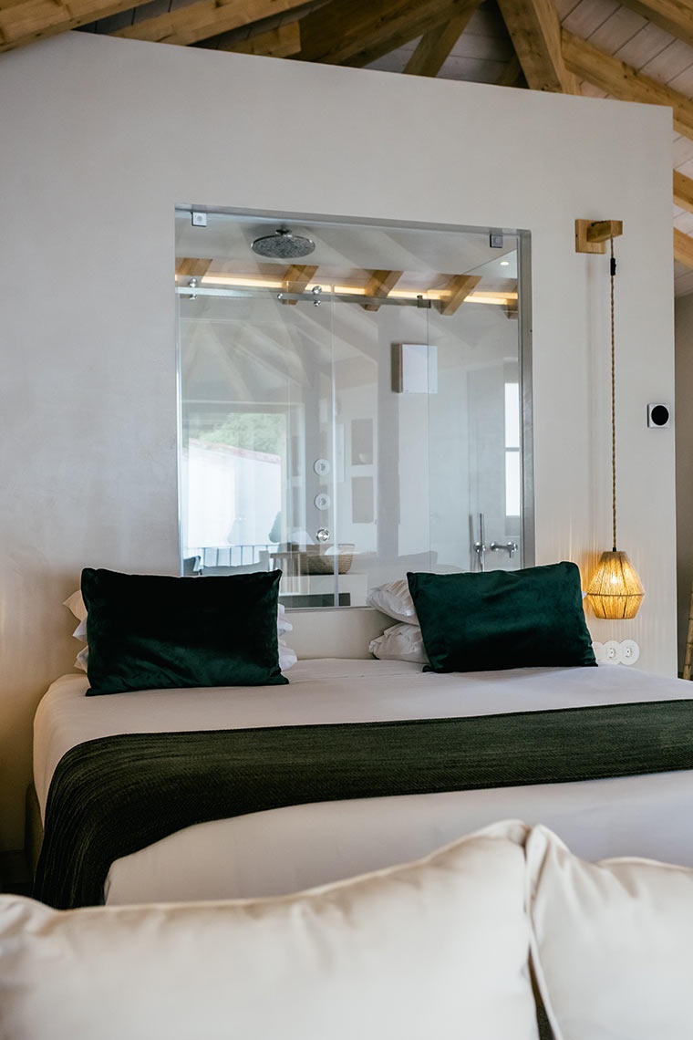 AndTales hotel suite: modern bedroom with glass shower enclosure, plush pillows, and natural light.