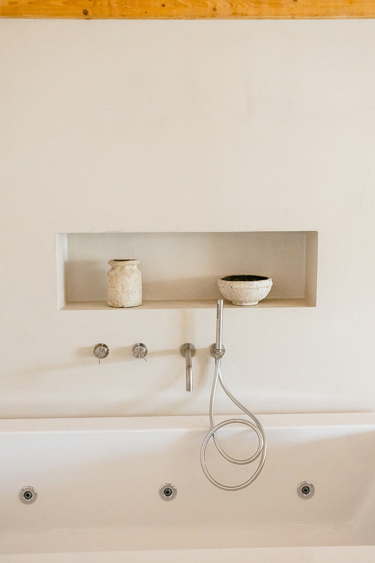 AndTales spa tub with modern fixtures and decorative bowls in recessed wall niche.