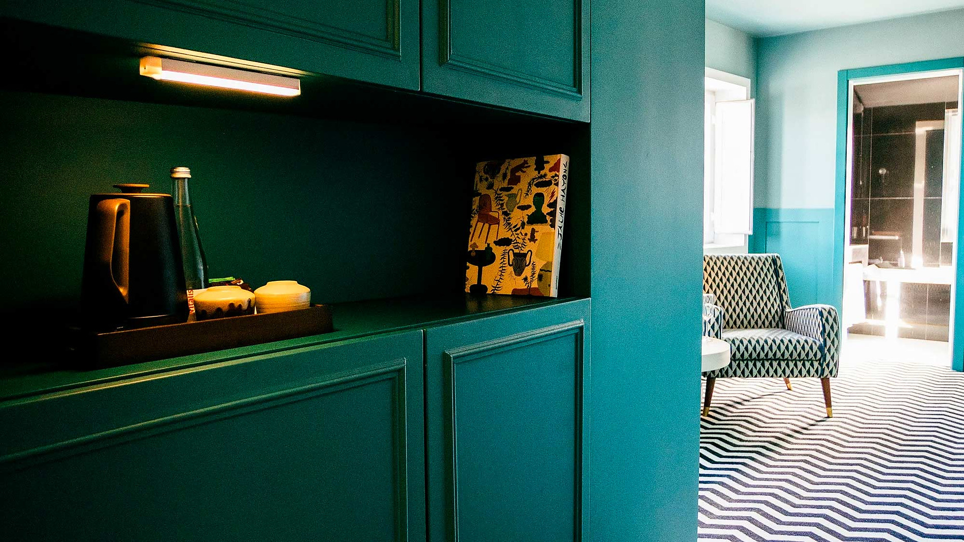 Design do quarto AndTales: móveis verdes escuros, tapete chevron e poltrona.
