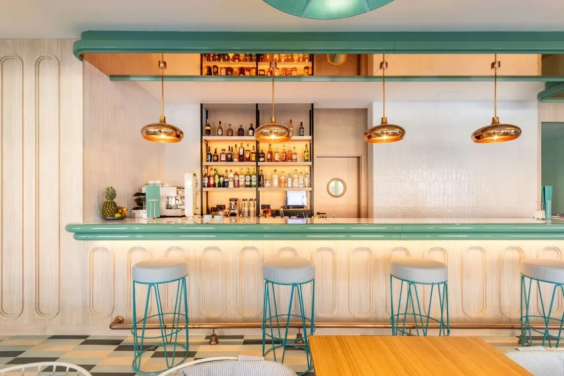 Bar moderne de l'hôtel Angela avec tabourets et bouteilles d'alcool.