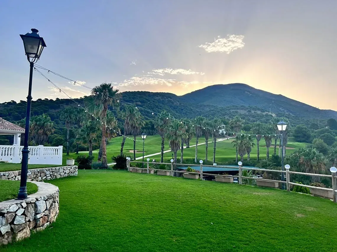 Ángela's resort: césped verde, palmeras y montaña al atardecer.