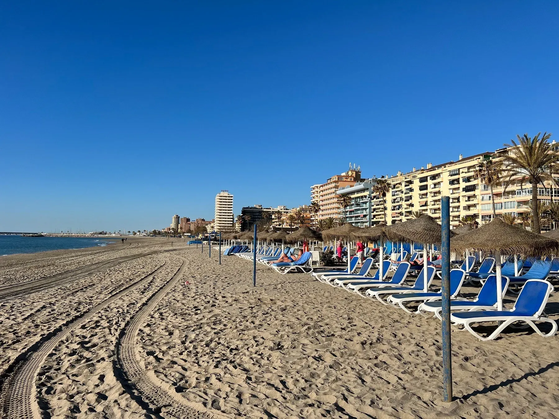 Angela's beach, blue loungers, and modern buildings under the sun.