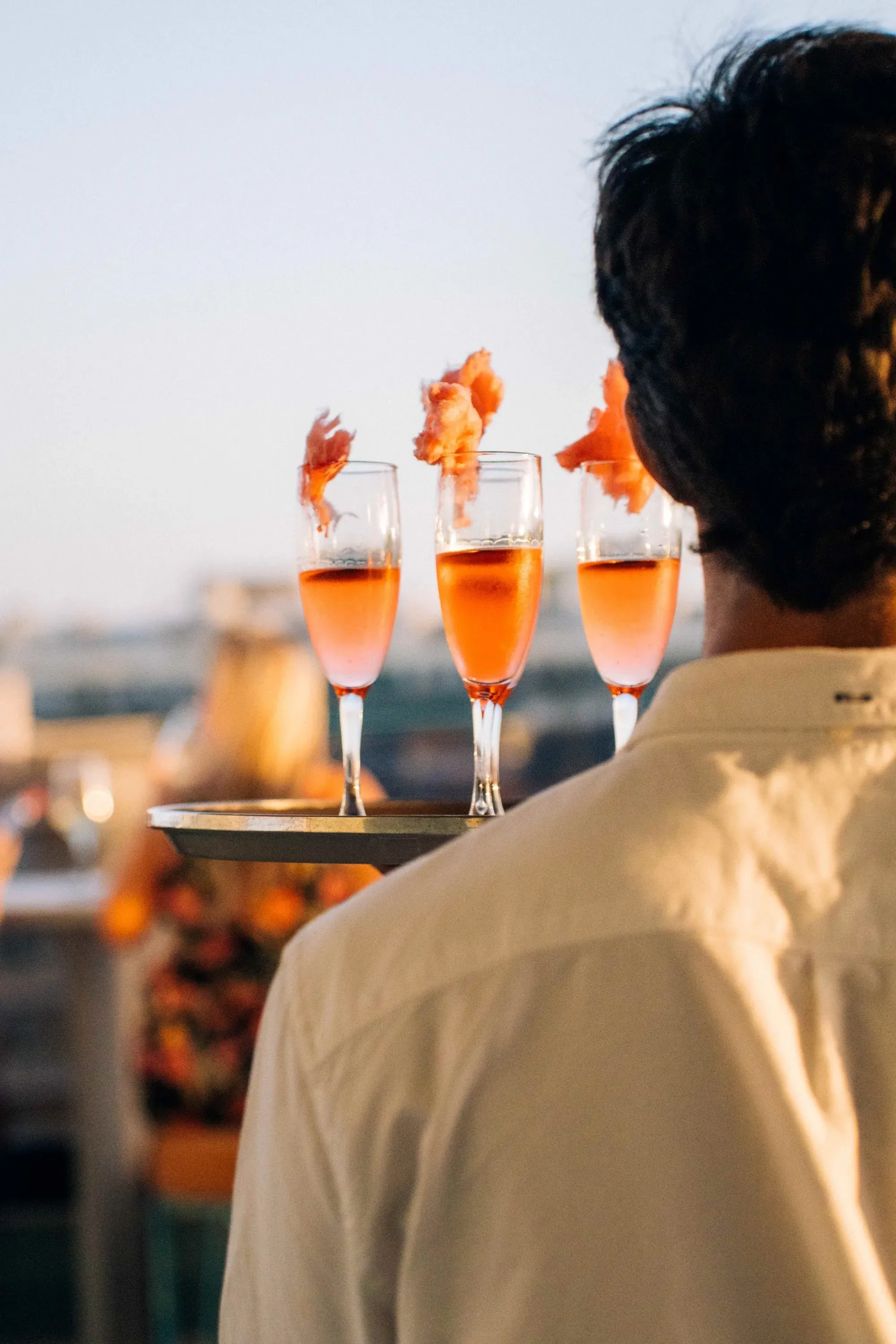 Waiter carries tray of pink cocktails, Angela's service.
