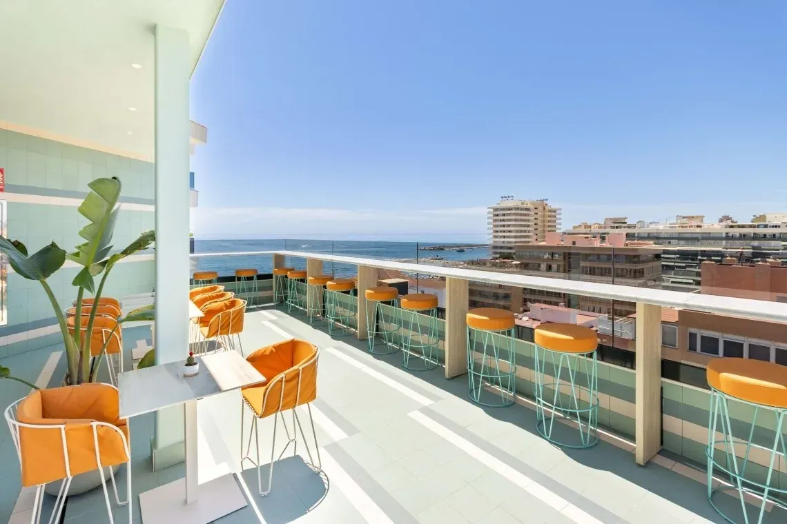 Terraza de Angela Hotel con vistas al mar y asientos naranjas.