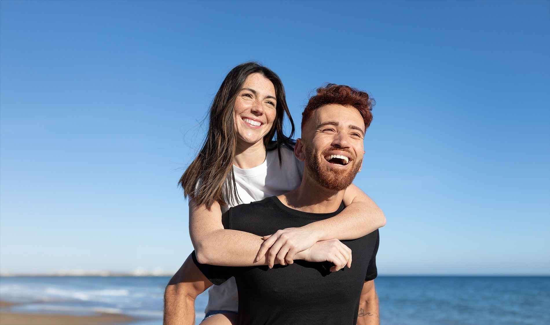 un hombre lleva a una mujer a cuestas en la playa