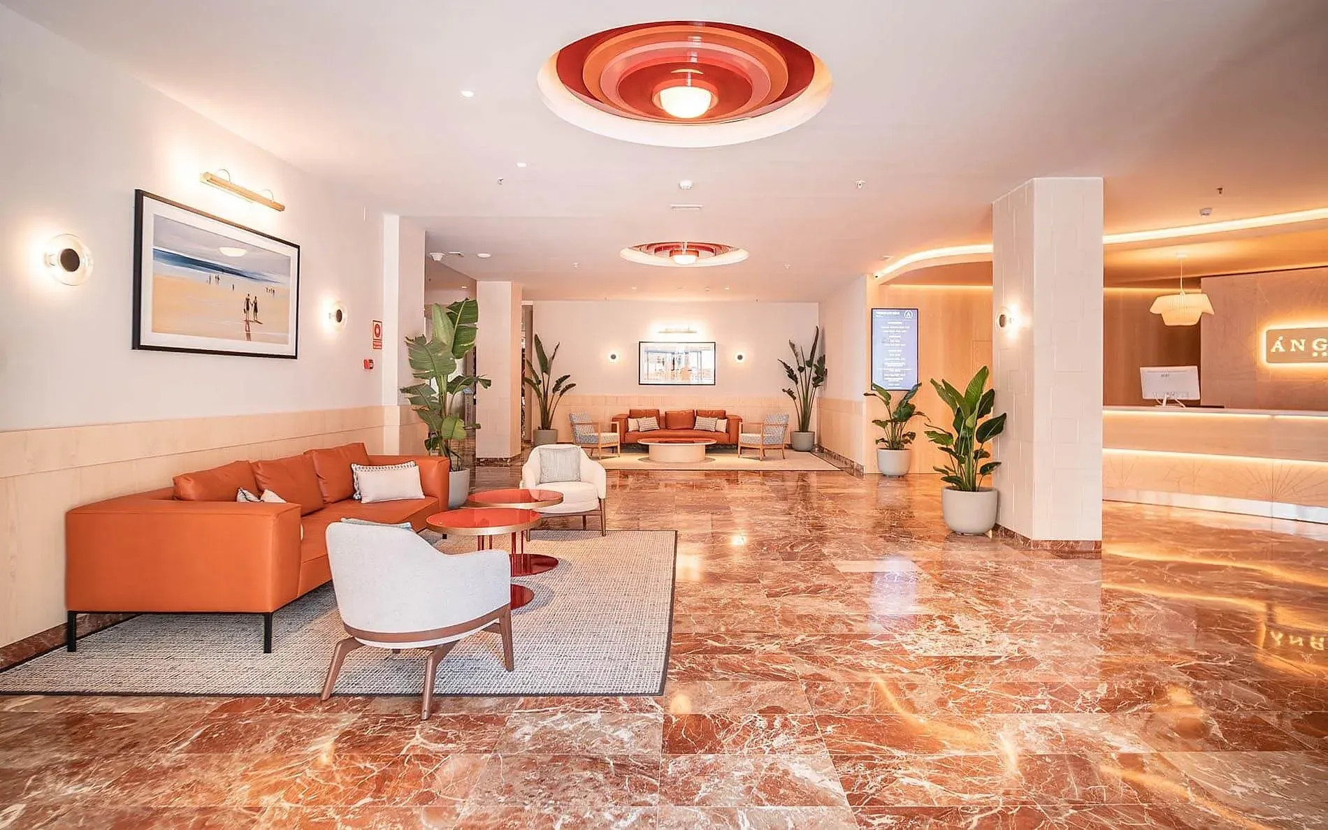 Galería | Hotel Ángela: Sofá naranja, sillas y suelo de mármol en el lobby. Web Oficial