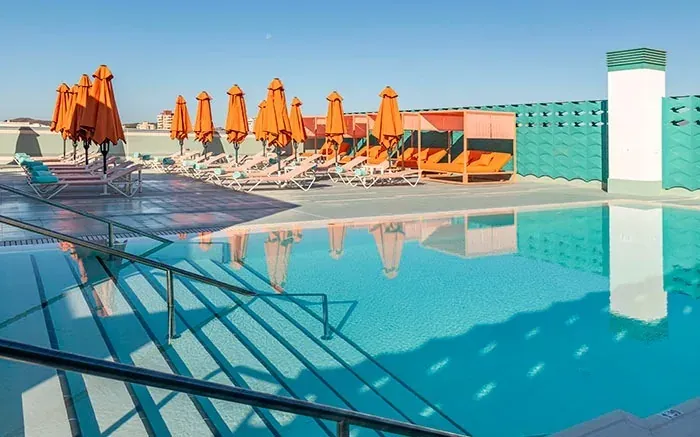 Piscina Angela en azotea con tumbonas y sombrillas naranjas.