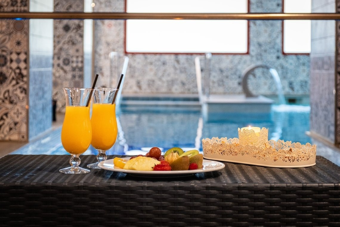 two glasses of orange juice and a plate of fruit sit on a table in front of a swimming pool