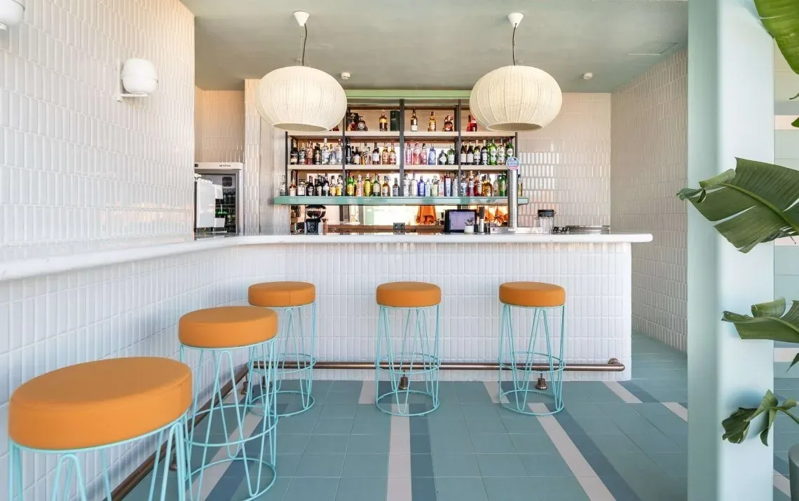 Bar moderne avec tabourets orange et sol bleu, parfait pour une Angela.