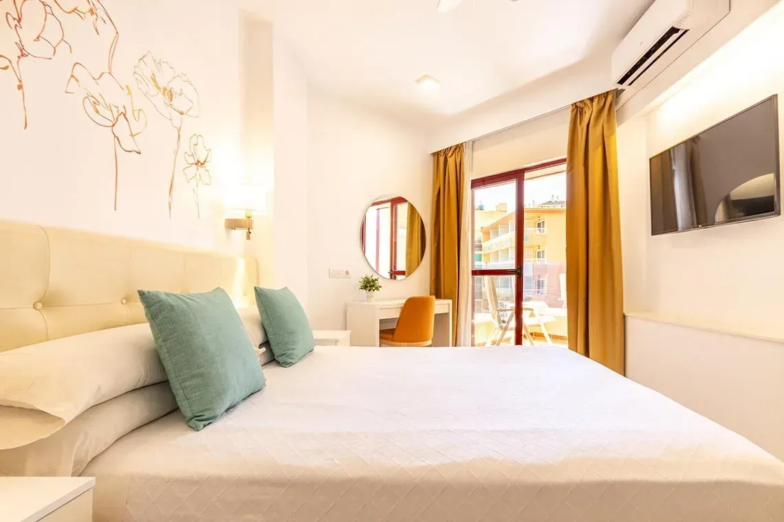 Habitación de hotel Angela con cama king y balcón soleado.