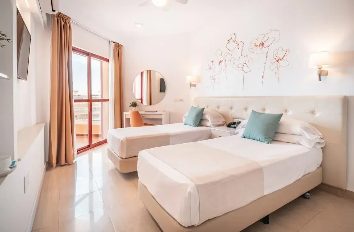 Habitación Angela con dos camas individuales, balcón y decoración floral.
