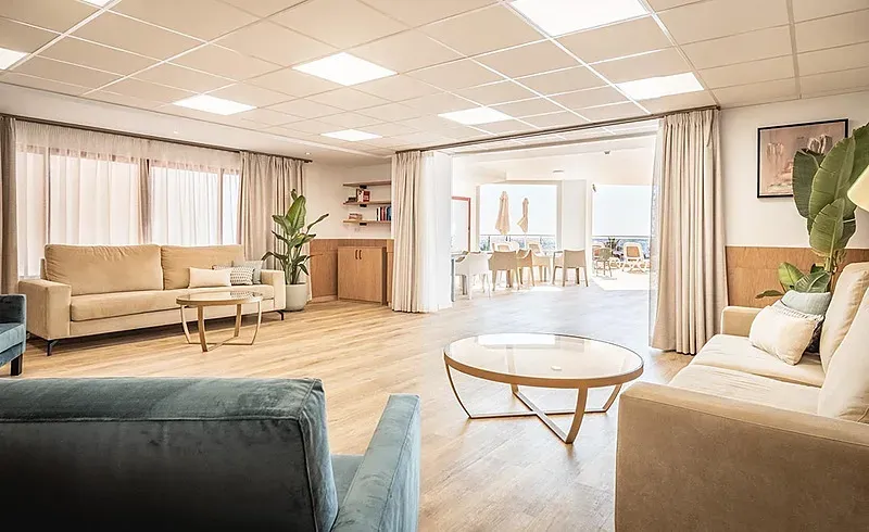 Salon lumineux et moderne de l'Hôtel Angela avec canapés et tables. Idéal pour se détendre.