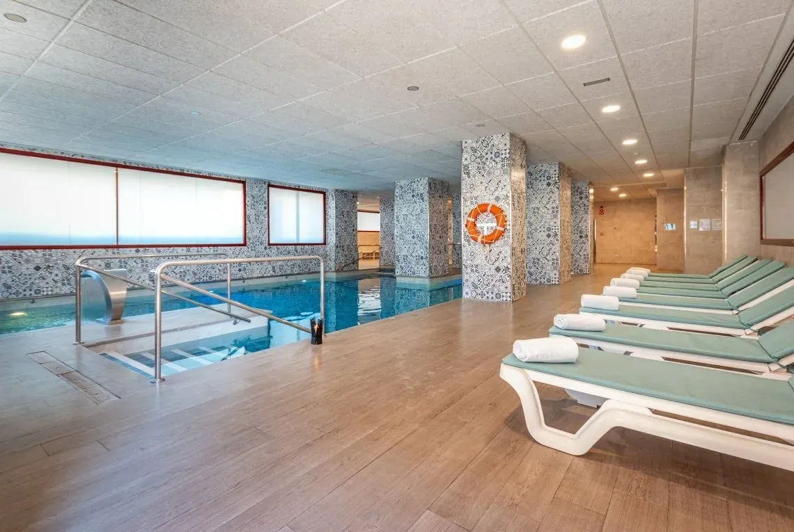 Piscina interior de hotel Ángela con tumbonas y decoración moderna.