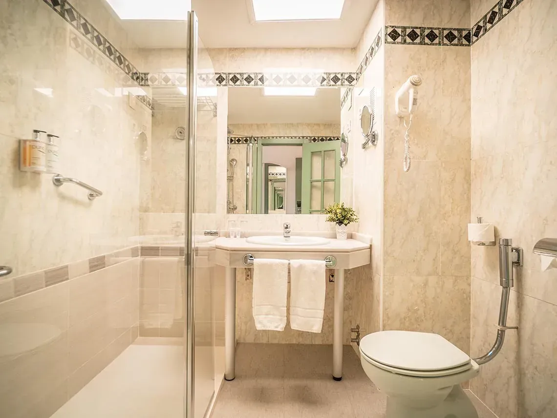 Baño moderno Angela con ducha, lavabo e inodoro, decorado con azulejos claros.