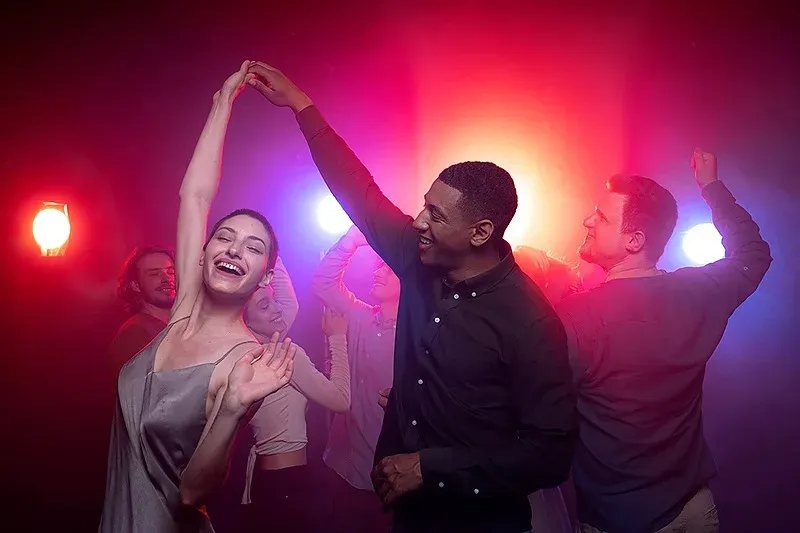 Angela danse joyeusement à la fête de l'hôtel avec des néons.