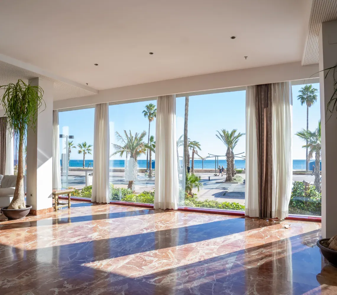 Lobby Angela: vistas al mar con palmeras y suelo de mármol brillante.