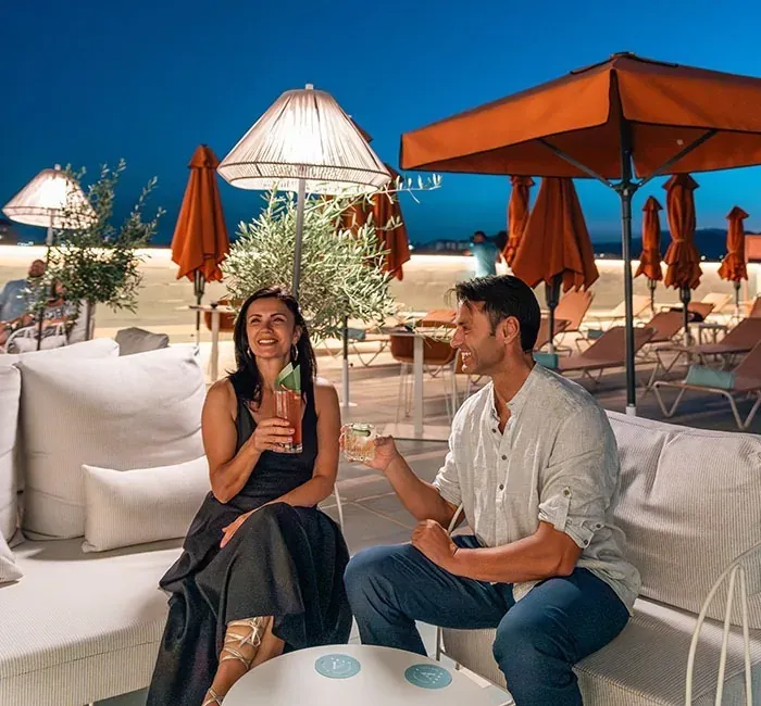 Pareja disfrutando cócteles bajo las sombrillas naranjas de Angela's Resort.