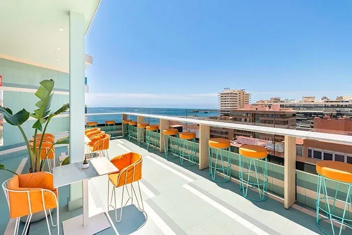 Terraza del Hotel Angela: vista al mar con sillas y mesas naranjas.