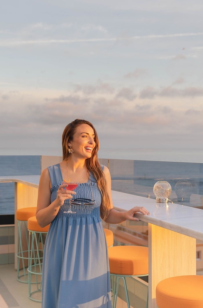 una mujer con un vestido azul sostiene un cóctel y sonríe