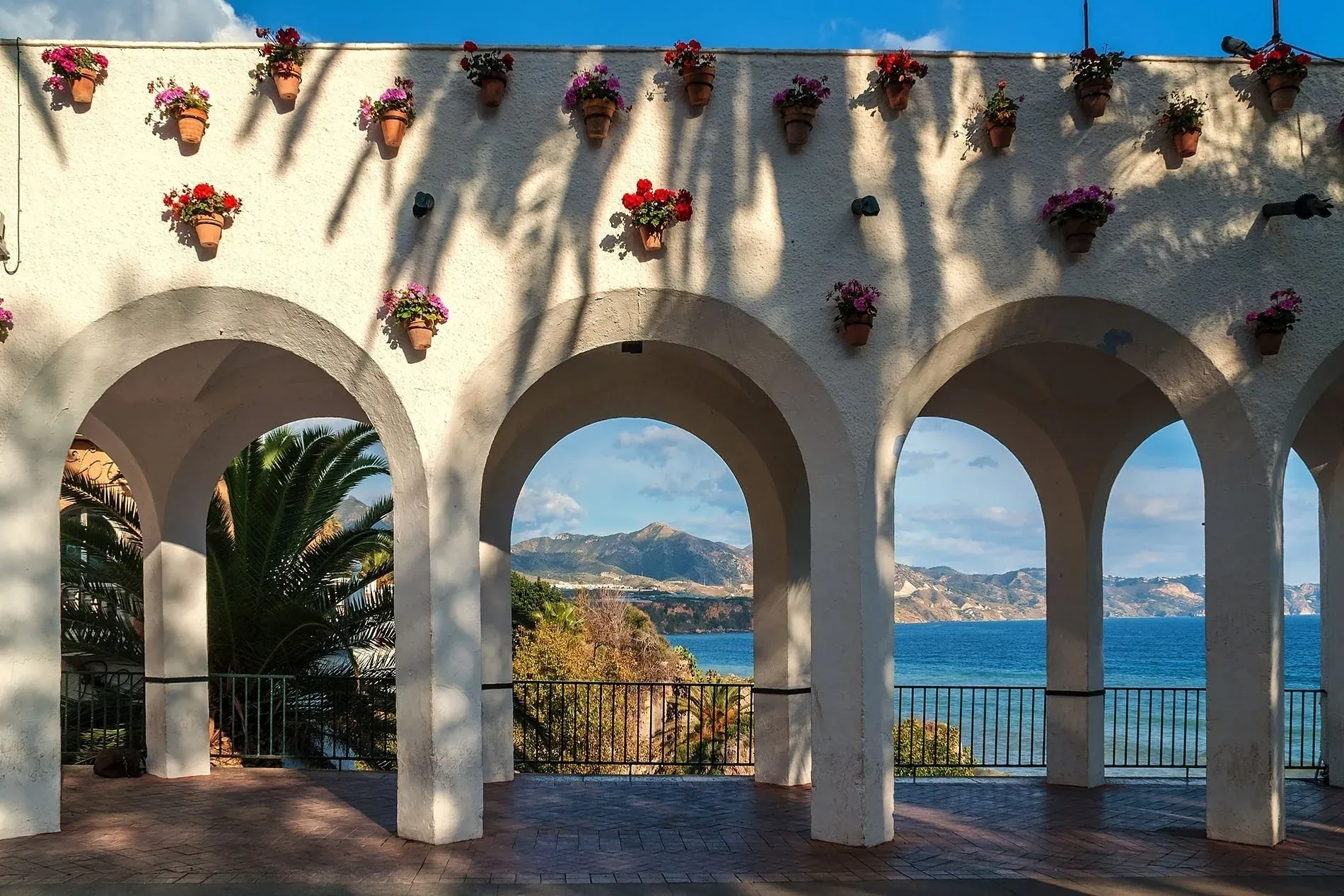 Visitez Nerja | Blogue | Hôtel Angela | Fuengirola | Costa del Sol : terrasse avec vue mer, balcons fleuris, arches blanches.