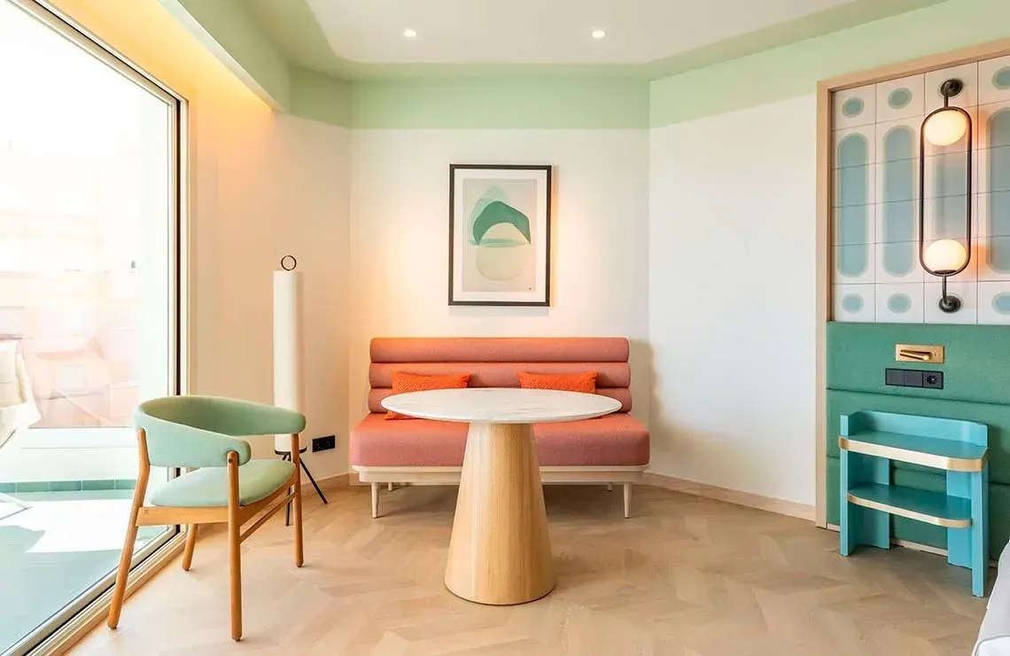 Habitación de hotel Angela: sofá coral, mesa mármol, silla verde y lámpara.