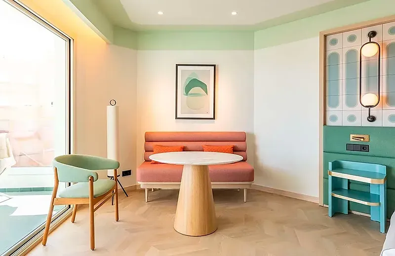 Habitación de hotel Angela: sofá coral, mesa mármol, silla verde y lámpara.