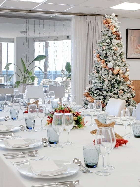 una mesa con platos y copas y un árbol de navidad en el fondo