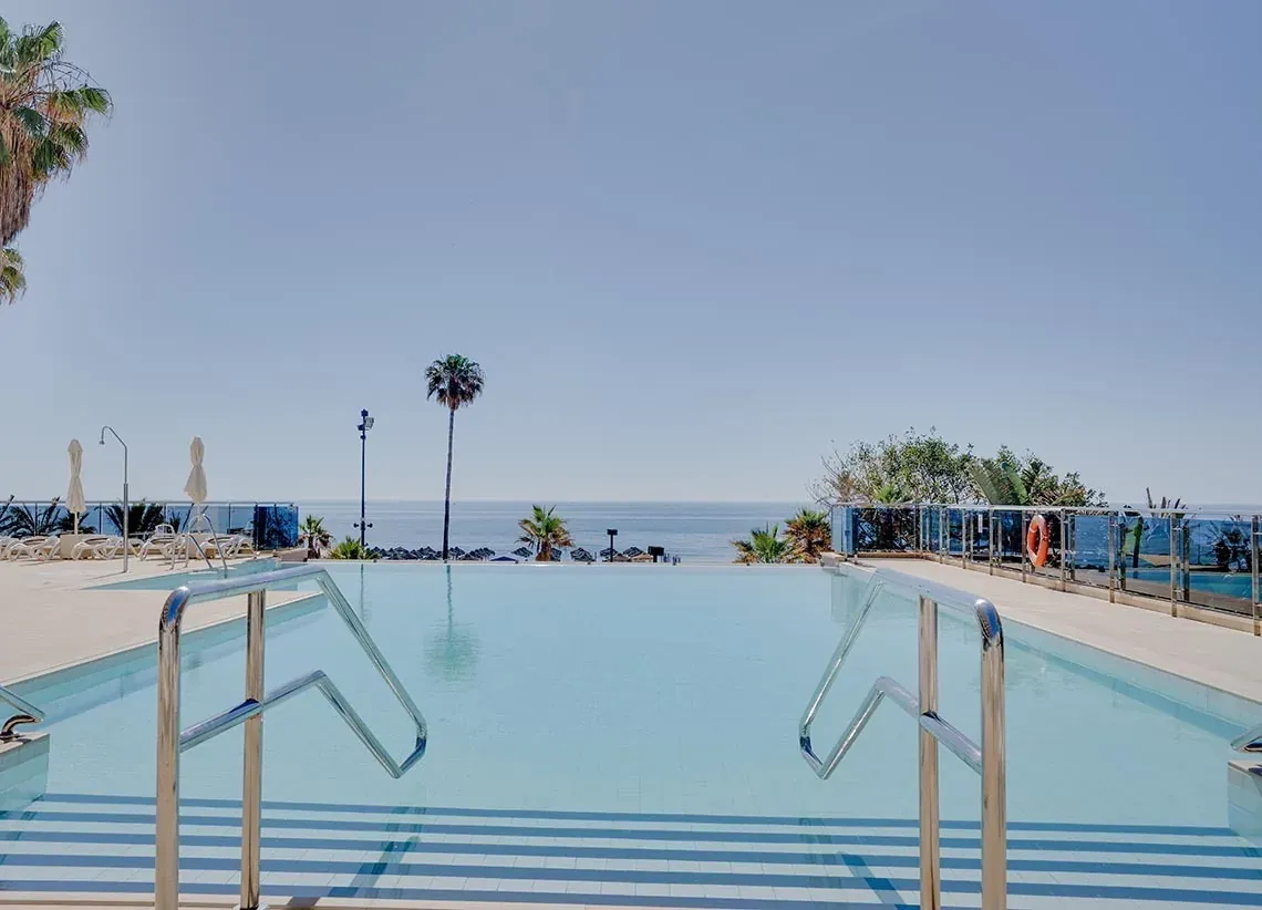 Piscine à débordement avec vue sur mer et palmiers, l'oasis d'Angela.