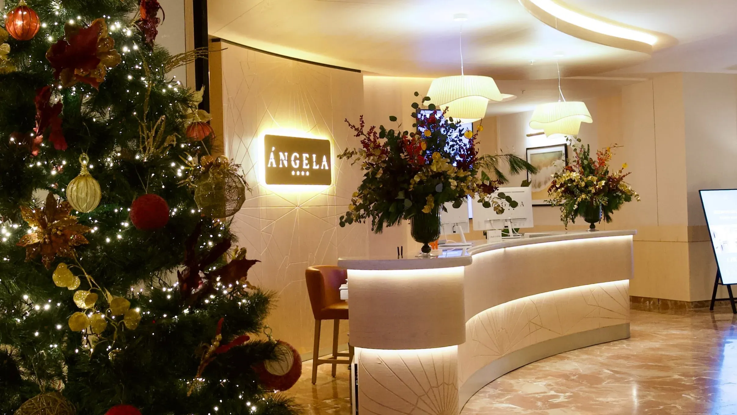 Réception de l'Hôtel Angela avec sapin de Noël festif et décor floral.