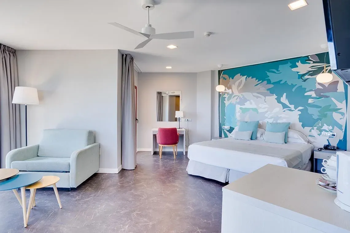 Habitación doble Angela con cama matrimonial, sofá y mural floral.