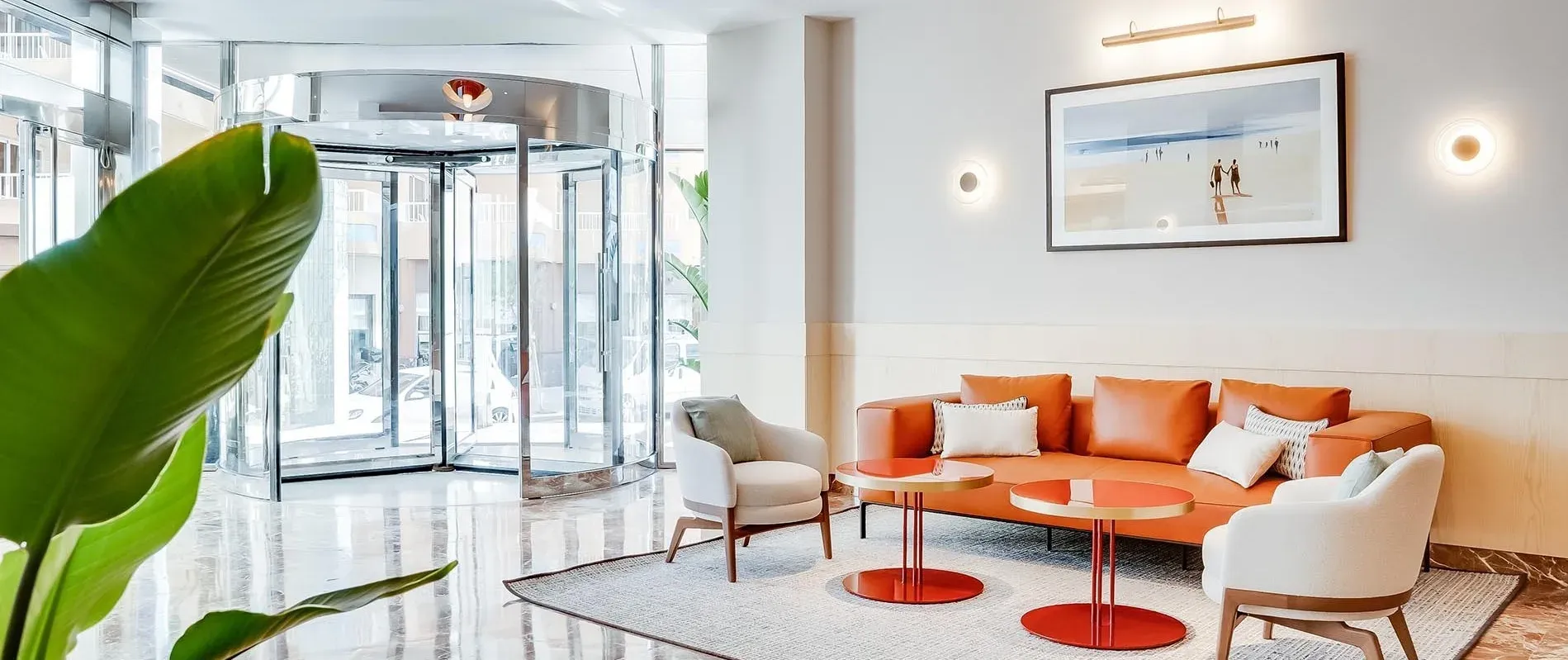 Lobby moderno del Hotel Ángela en Fuengirola, Costa del Sol, con sofás naranjas y plantas.