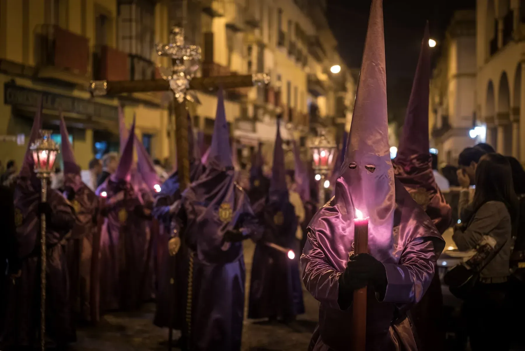 Procesión religiosa nocturna con nazarenos morados, velas y cruz, evocando la Semana Santa Angelical.