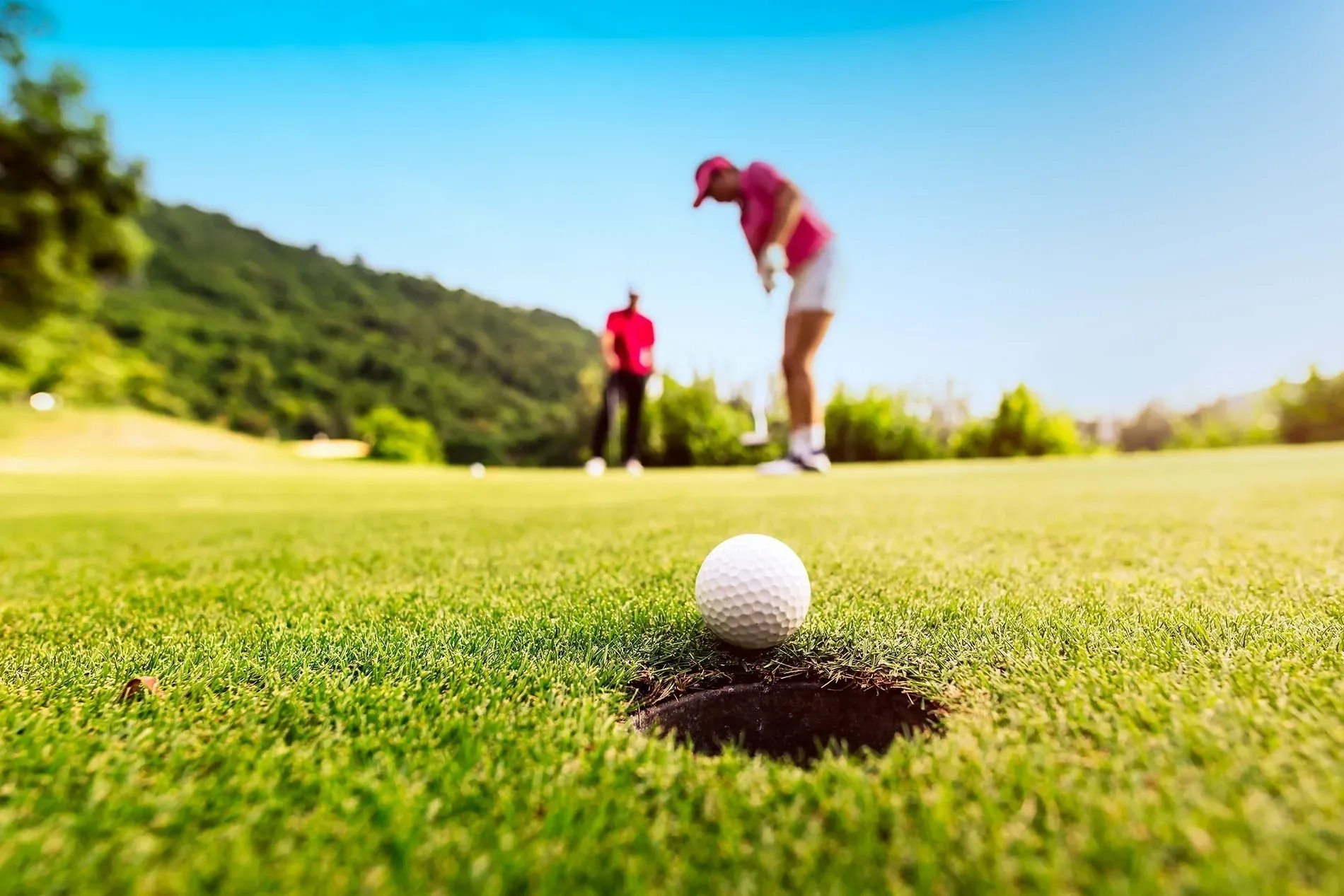 Juega al golf en la Costa del Sol. Golfistas en campo verde con hoyo y pelota. Blog Hotel Ángela Fuengirola.