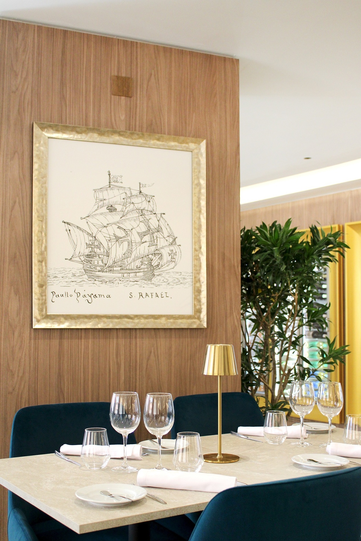 una mesa de comedor con copas de vino y un dibujo de un barco en la pared