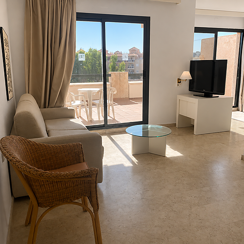 Salón de hotel con sofá, mesa de centro y terraza acristalada. AR: Almerimar