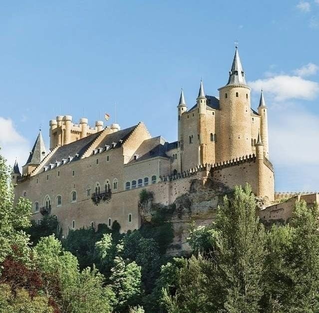 un gran castillo está sentado encima de una colina rodeada de árboles .